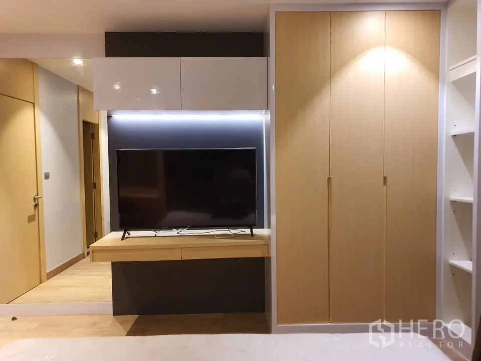 Condominium for rent in Watthana, Bangkok - Bedroom with built-in TV wall, floating shelf, light-wood wardrobe and side shelving.