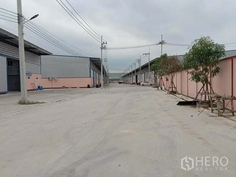 โรงงาน ให้เช่าในBan Phaeo, Samut Sakhon - ถนนคอนกรีตกว้างระหว่างอาคารโรงงานโครงเหล็กพร้อมสายไฟเหนือศีรษะ ในอำเภอเมืองสมุทรสาคร