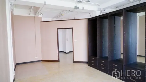 办公空间 出租在Watthana, Bangkok - 转角办公区，带门洞与高立式收纳柜，浅色墙面与外露线管。