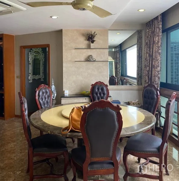 Condominium for rent in Khlong Toei, Bangkok - Dining room with round marble table, upholstered chairs and city-view windows.