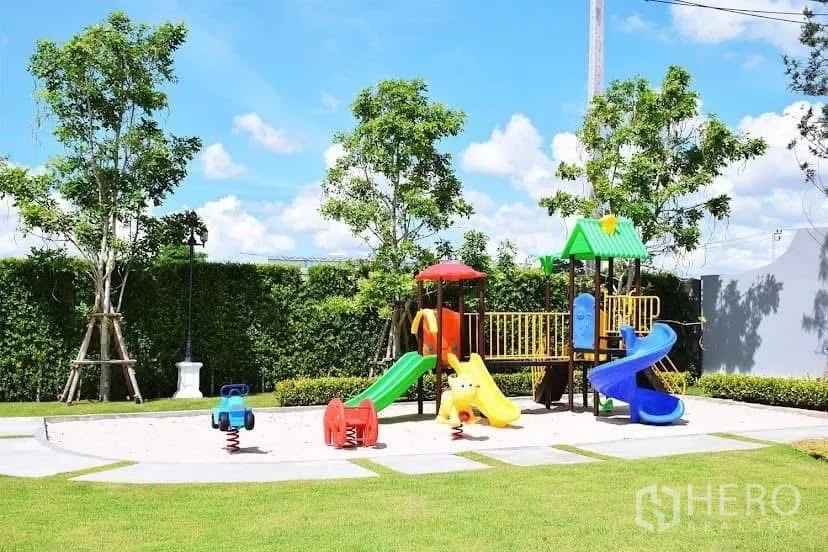 独立式住宅 出租在Prawet, Bangkok - 小区儿童乐园，彩色滑梯与弹簧摇马，周围是草坪与树木。