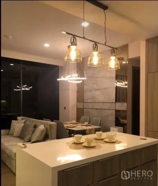 คอนโด ให้เช่าในWatthana, Bangkok - ห้องครัวแบบเปิดพร้อมไอส์แลนด์ โคมไฟแขวนแก้ว และมุมมองไปยังพื้นที่รับประทานอาหารและนั่งเล่น