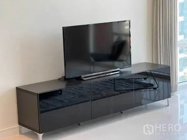 Condominium for rent in Watthana, Bangkok - Modern living room TV on glossy black media console beside full-height window.