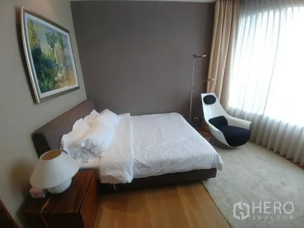 Condominium for rent or sale in Watthana, Bangkok - Master bedroom with large window, accent chair, sheer curtains, and wood floor.