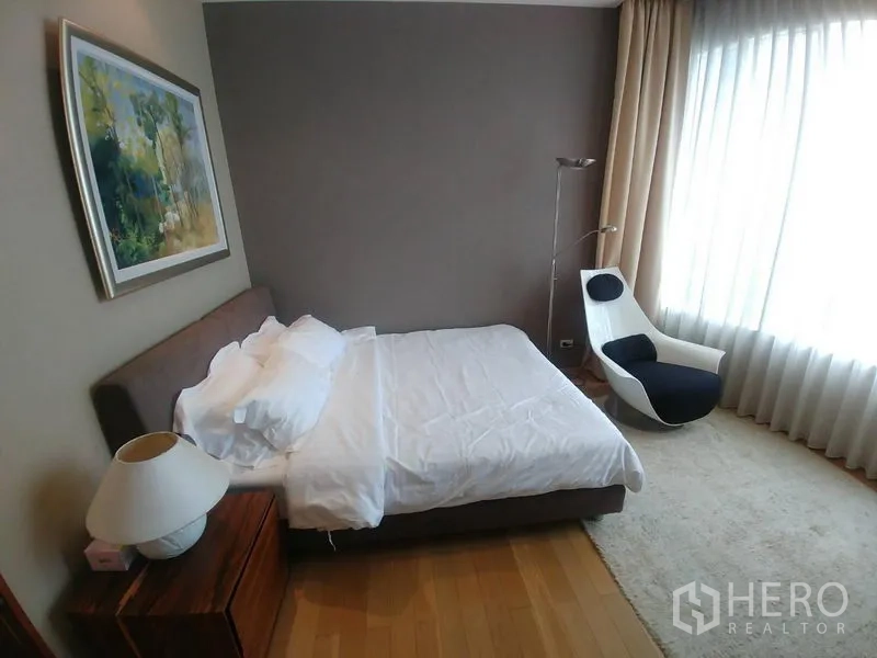 Condominium for rent or sale in Watthana, Bangkok - Master bedroom with large window, accent chair, sheer curtains, and wood floor.