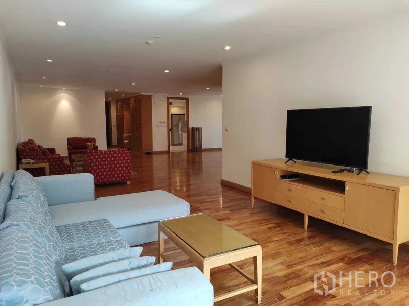 Condominium for rent in Khlong Toei, Bangkok - Living room with blue sectional sofa, TV console and coffee table under recessed lighting.