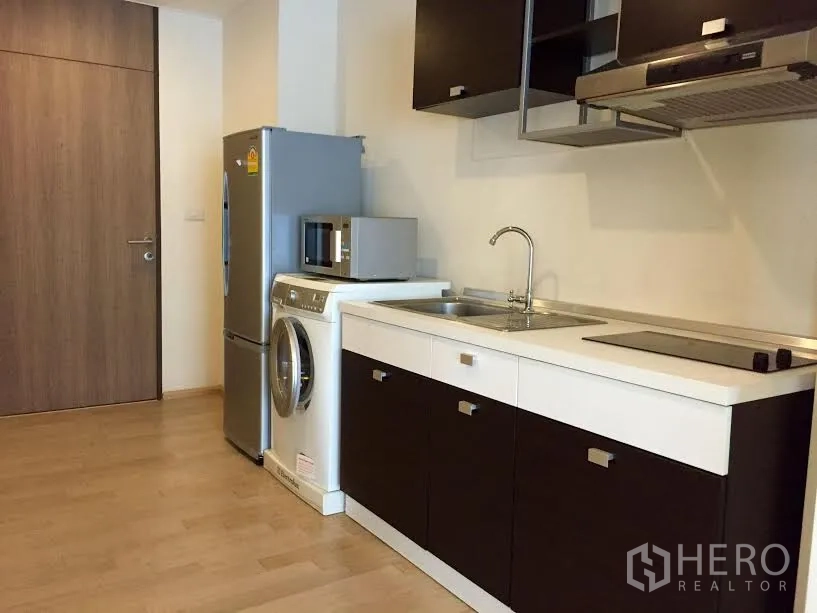 Condominium for rent or sale in Khlong Toei, Bangkok - Compact kitchen with sink, electric cooktop, range hood, fridge, washer, and microwave in a modern condo.