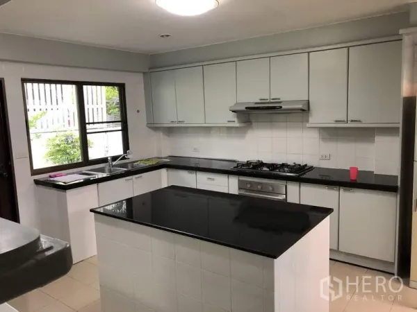 Detached House for rent in Khan Na Yao, Bangkok - Bright U-shaped kitchen with white cabinetry, gas hob, center island and black granite countertops.