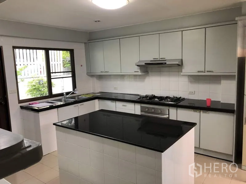 Detached House for rent in Khan Na Yao, Bangkok - Bright U-shaped kitchen with white cabinetry, gas hob, center island and black granite countertops.