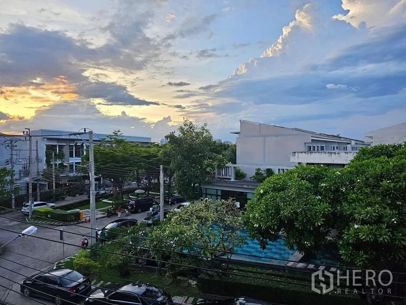 联排别墅 出租在Wang Thonglang, Bangkok - 阳台眺望绿意社区与泳池，傍晚天空景色。