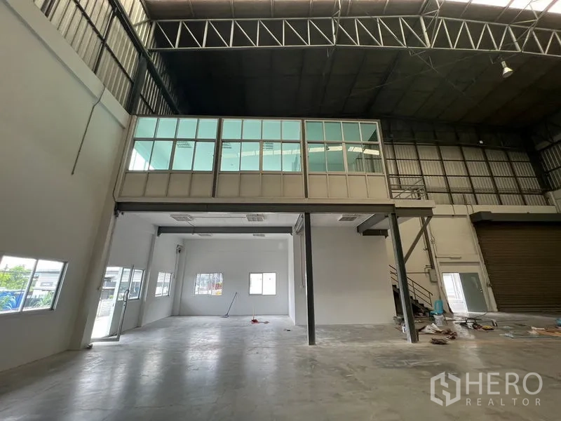 Warehouse for rent in Lat Krabang, Bangkok - Glass-walled mezzanine office overlooking the warehouse, with stairs and nearby roller shutter.