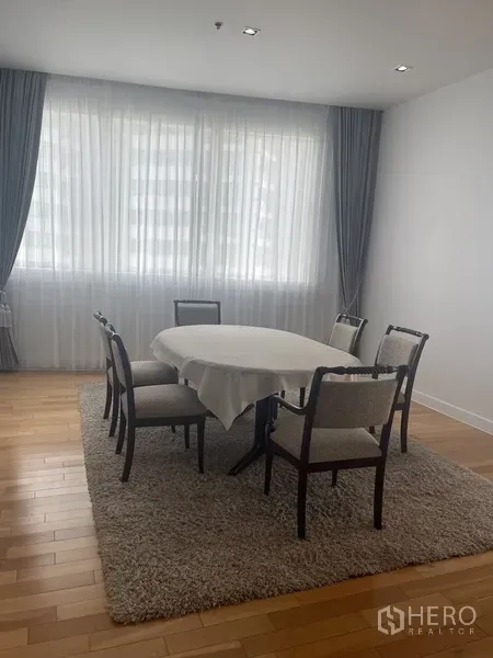 Condominium for rent in Khlong Toei, Bangkok - Dining area with a six-seat round table, soft curtains and a wide window.