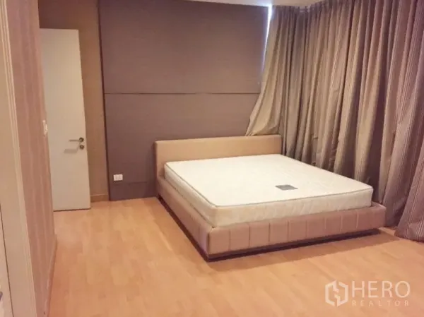 Condominium for rent in Khlong Toei, Bangkok - Master bedroom with platform bed, wood flooring, and floor-to-ceiling drapes.