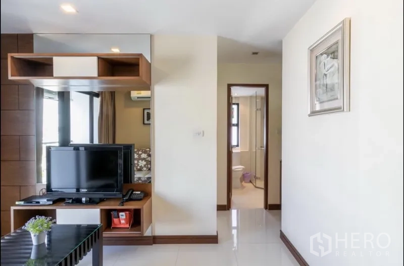 房间 出租在Bang Rak, Bangkok - 从客厅望向浴室的走廊视角，可见电视柜与置物架。