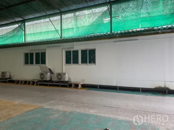 Warehouse for rent in Lam Luk Ka, Pathum Thani - Side elevation with windows, AC compressors and shade net over loading area