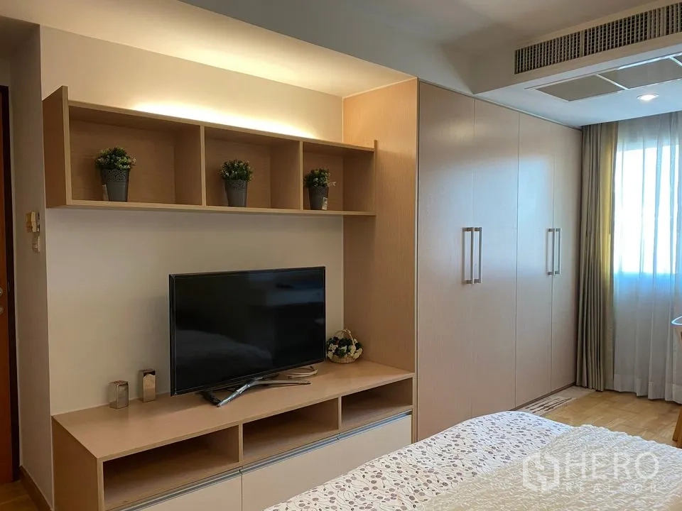 Condominium for rent or sale in Phra Khanong, Bangkok - Bedroom with TV console, open shelves and large built-in wardrobe in light wood tones.