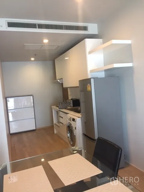 Condominium for rent in Bangkok - Compact galley kitchen with white cabinetry, refrigerator, microwave and washing machine beside the dining table.