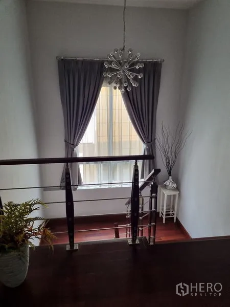 Detached House for sale in Chatuchak, Bangkok - Stair landing with chandelier, gray drapes and a metal-and-wood railing.