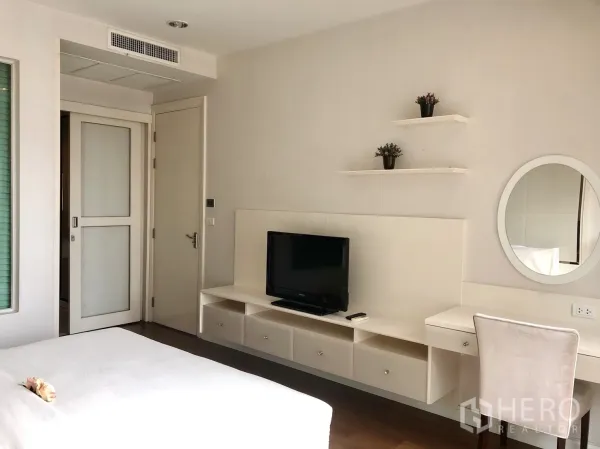 公寓 出租在Pathum Wan, Bangkok - 卧室带内置书妆一体桌与搁板，墙挂电视，配色柔和。
