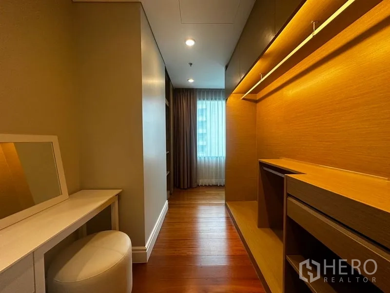 Condominium for rent in Khlong Toei, Bangkok - Walk-in closet with built-in shelves and dressing table under warm lighting.