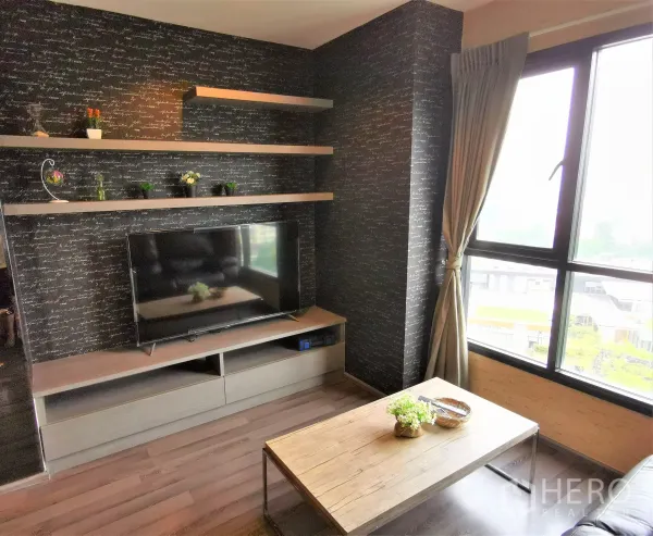 Condominium for rent or sale in Watthana, Bangkok - Entertainment wall with floating shelves and flat-screen TV next to curtained window and coffee table.