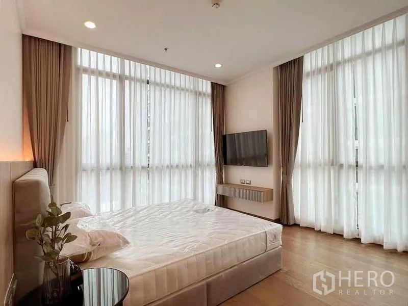 คอนโด ให้เช่าในWatthana, Bangkok - ห้องนอนมุมอาคาร หน้าต่างสูงรอบด้าน ผ้าม่านโปร่ง ทีวีติดผนัง และพื้นไม้