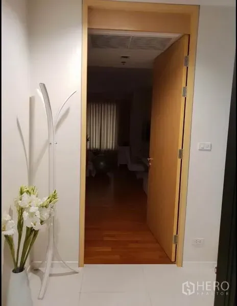 Condominium for rent in Sathon, Bangkok - Entrance hallway with open wooden door, white tiles and a decorative flower vase.