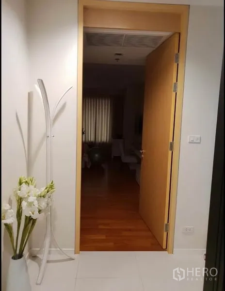 Condominium for rent in Sathon, Bangkok - Entrance hallway with open wooden door, white tiles and a decorative flower vase.