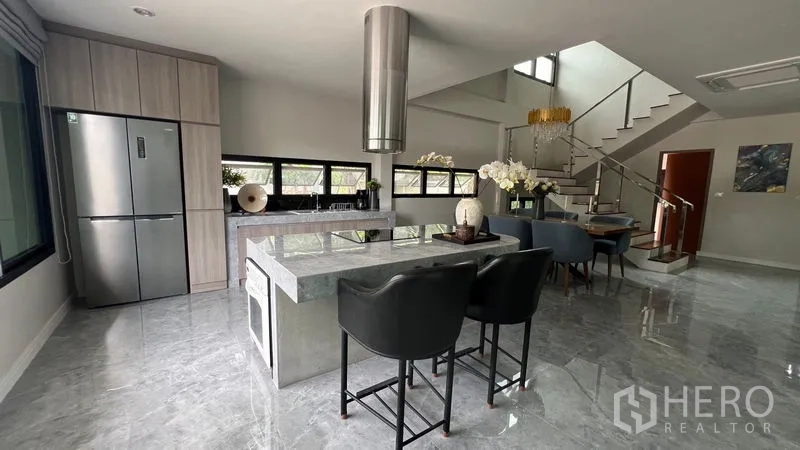 独立式住宅 出租在Lat Krabang, Bangkok - 开放式厨房，石材中岛、不锈钢烟机与吧椅，连接楼梯。