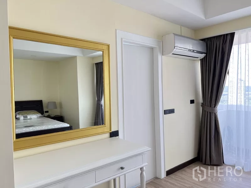 Condominium for rent in Khlong Toei, Bangkok - Dressing nook with gold-framed mirror, white console table, AC unit and curtained window.