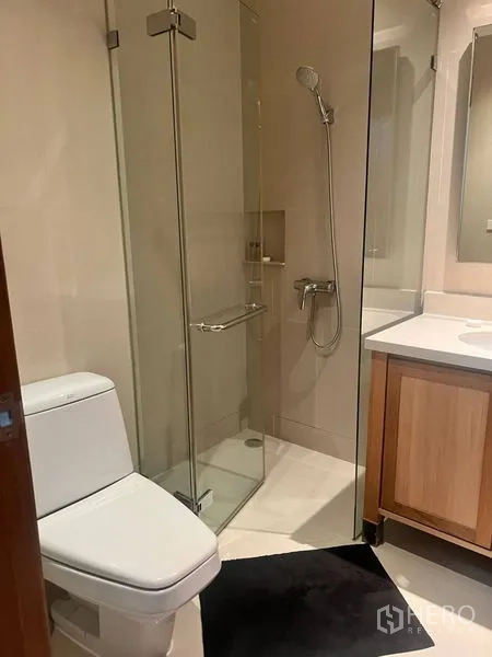 公寓 出租在Bangkok - 现代浴室，玻璃淋浴间、马桶与木质洗手台。