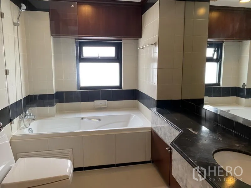 Condominium for rent or sale in Sathon, Bangkok - Bathroom with soaking bathtub, long marble vanity and a window for natural light.