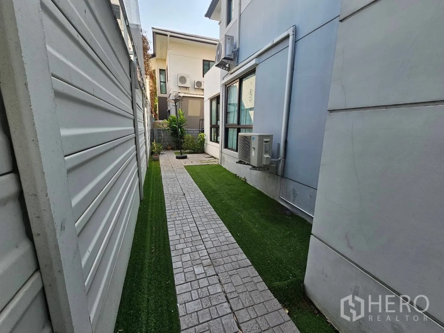 Detached House for rent or sale in Wang Thonglang, Bangkok - Side yard with paved path, artificial grass and exterior air-conditioning units.