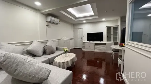 房间 出租在Watthana, Bangkok - 明亮客厅，灰色L型沙发、灯槽天花、电视柜与亮泽实木地板。