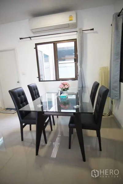 Townhouse for rent in Suan Luang, Bangkok - Glass-top dining table for four beneath a window and air conditioner.