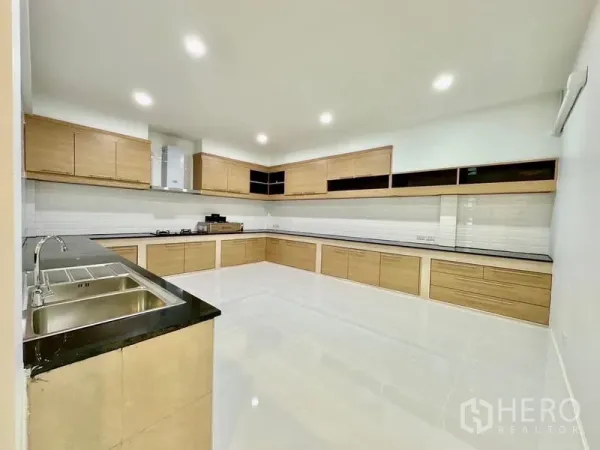 独立式住宅 出租在Lat Krabang, Bangkok - 宽敞泰式厨房，L形木质橱柜、白色墙砖与筒灯