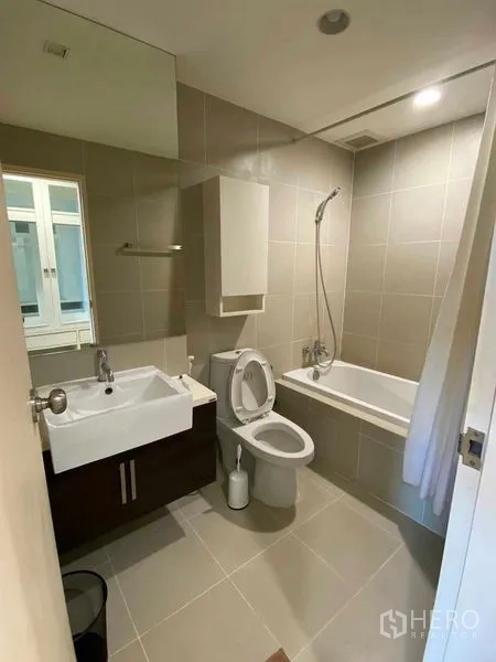 Condominium for rent in Khlong Toei, Bangkok - Second bathroom with bathtub, handheld shower, vanity and large wall mirror.