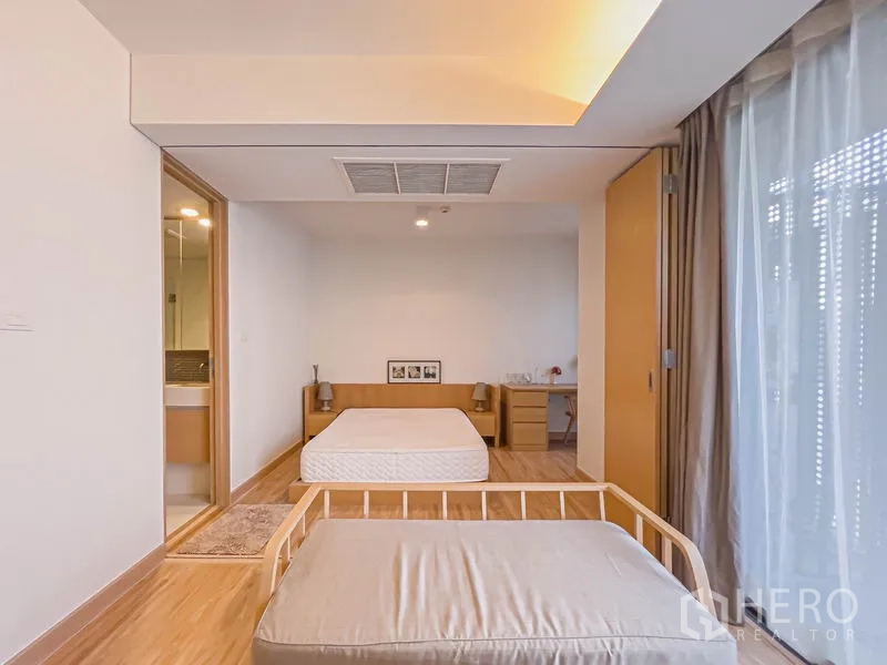 公寓 出售在Watthana, Bangkok - 卧室区设大床、床头柜和书桌，旁边是通往浴室的推拉门与高窗。