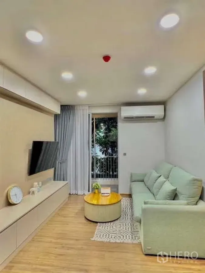 คอนโด ขายในWatthana, Bangkok - ห้องนั่งเล่นสว่างที่ Q Prasarnmit โซฟาสีเขียวอ่อน ทีวีติดผนัง และประตูกระจกสู่ระเบียง