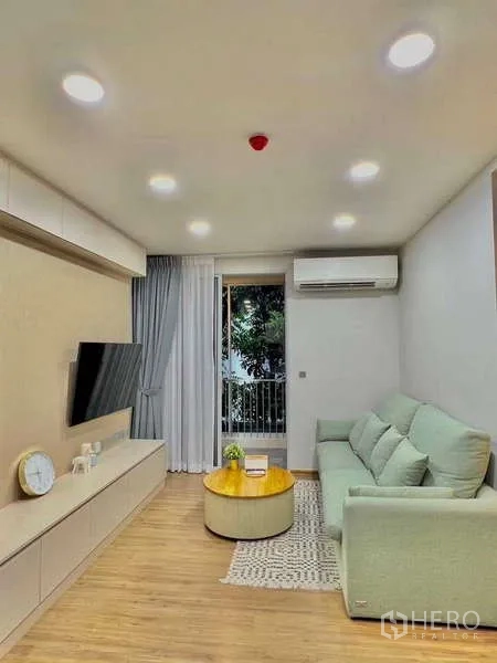 คอนโด ขายในWatthana, Bangkok - ห้องนั่งเล่นสว่างที่ Q Prasarnmit โซฟาสีเขียวอ่อน ทีวีติดผนัง และประตูกระจกสู่ระเบียง