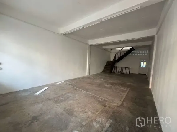 Shophouse for rent in Watthana, Bangkok - Open-plan ground floor space with high ceiling and concrete floor leading to staircase.