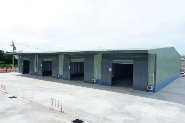 货栈 出租在Pak Kret, Nonthaburi - 新建排式仓库外观，宽大卷闸门与可供卡车使用的硬化场地