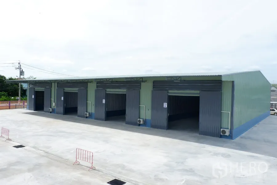 货栈 出租在Pak Kret, Nonthaburi - 新建排式仓库外观，宽大卷闸门与可供卡车使用的硬化场地
