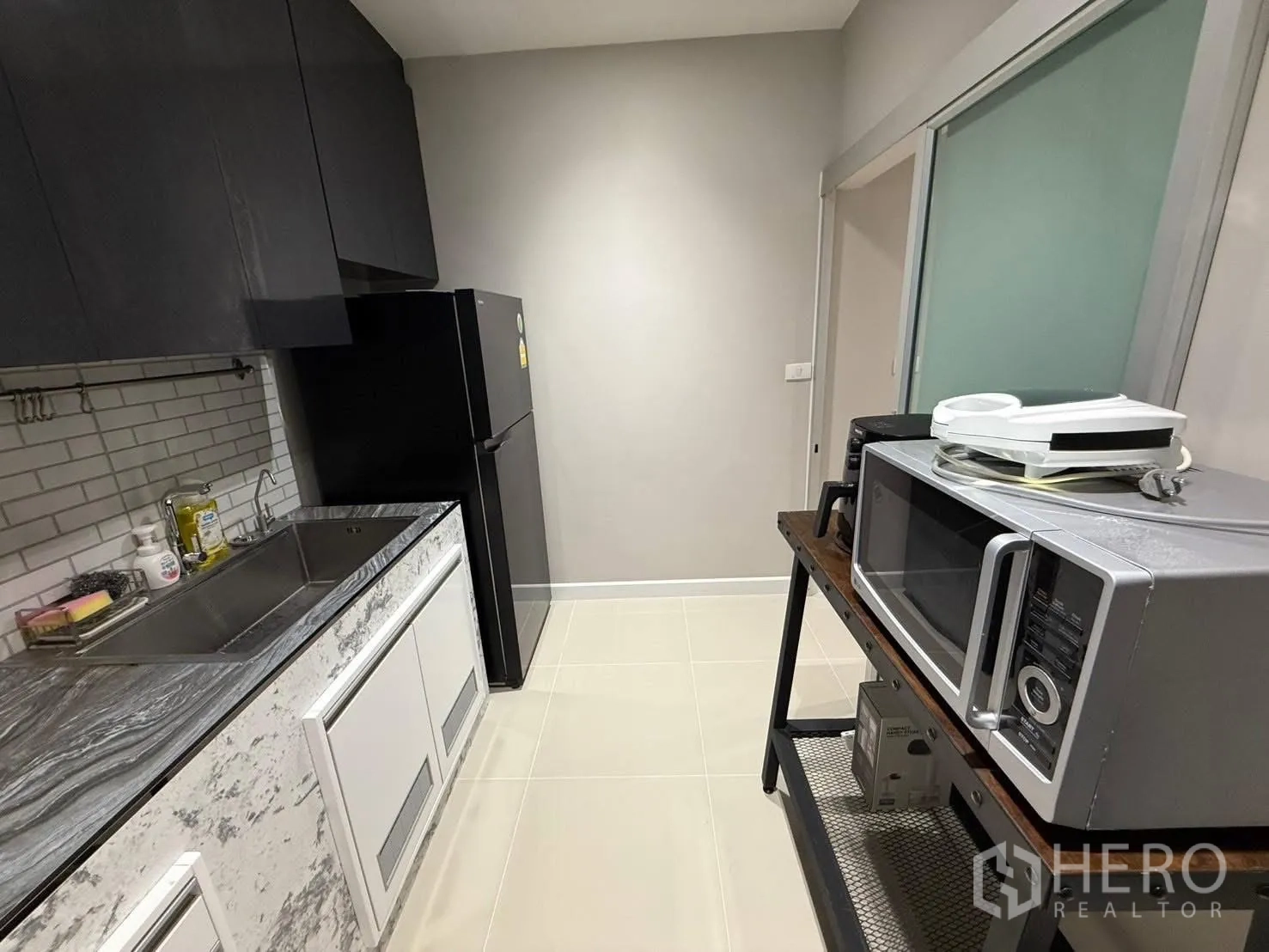 独栋房屋 for rent in Prawet, Bangkok - 封闭式小厨房，岩纹台面、不锈钢水槽、黑色橱柜与置物架上的微波炉