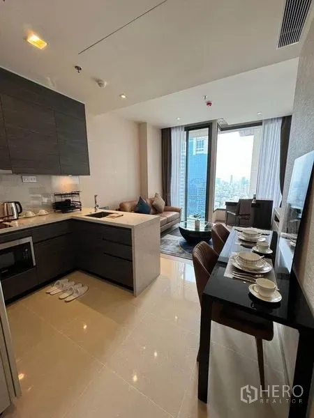 公寓 出租在Watthana, Bangkok - 开放式厨房配深色柜体，四人餐桌，与靠窗的起居区相连。