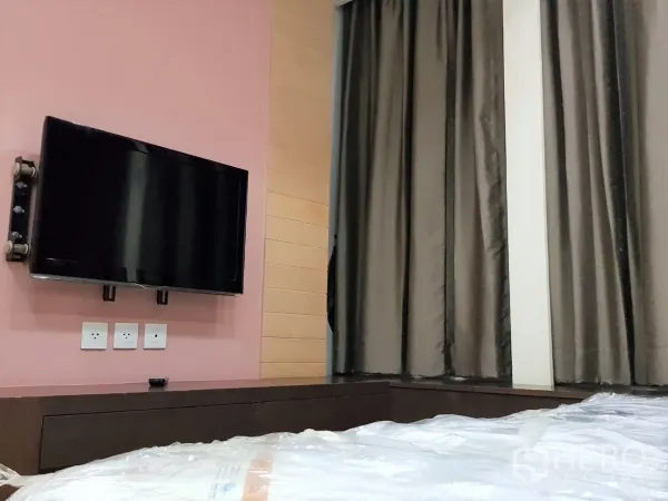 Condominium for rent in Khlong Toei, Bangkok - Master bedroom wall with mounted flat-screen TV and blackout curtains.