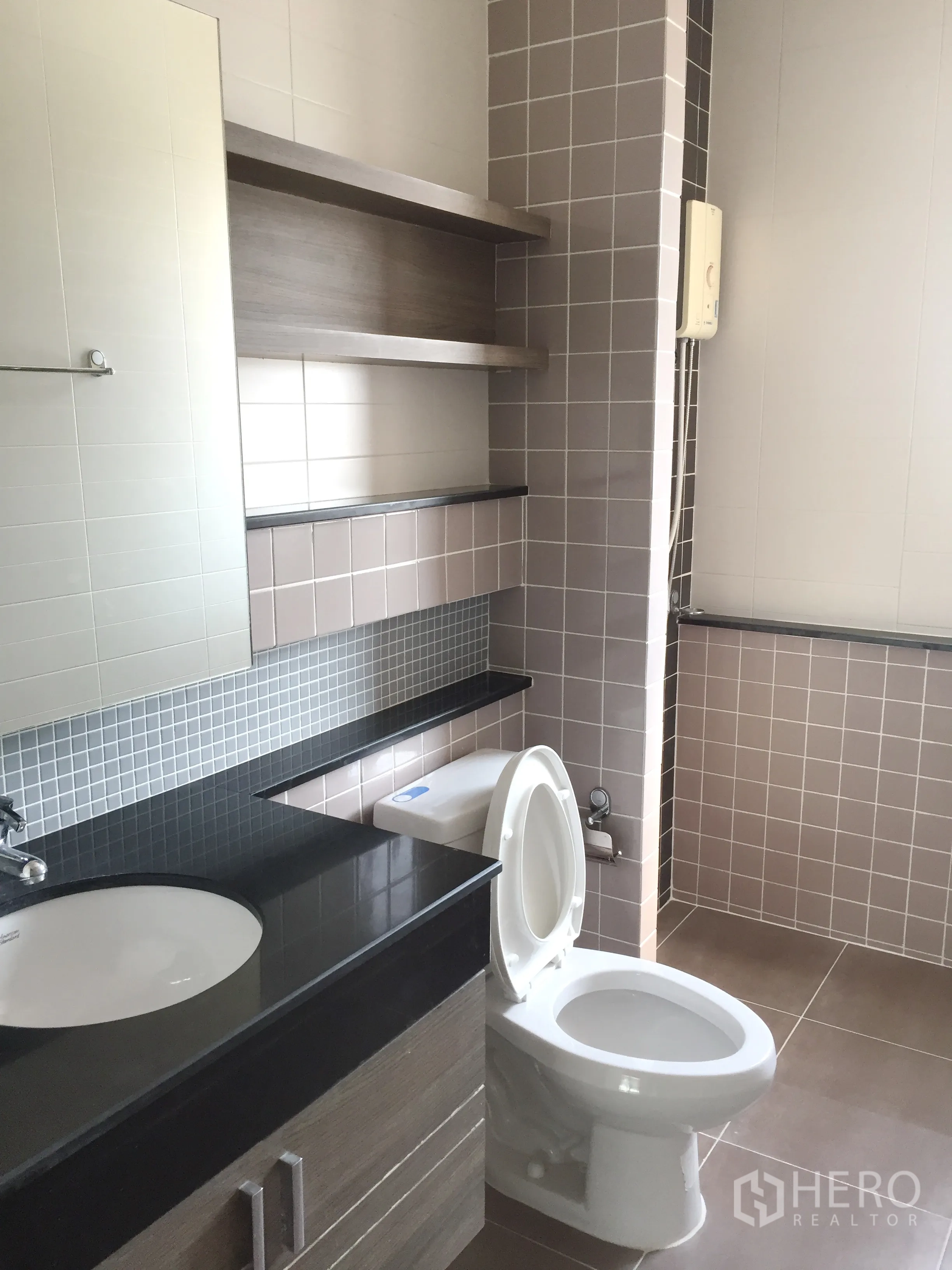 Townhouse for rent or sale in Phra Khanong, Bangkok - Bathroom with black stone vanity, shelves, toilet, and beige tiled walls.