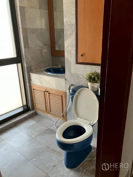 Condominium for rent in Watthana, Bangkok - Compact bathroom with blue toilet and sink beside a frosted window.