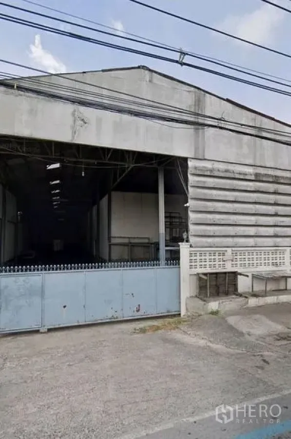 Warehouse for rent in Pathum Thani - Street-facing warehouse facade with wide sliding gate and concrete driveway in Mueang Pathum Thani.