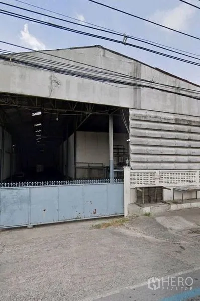 Warehouse for rent in Pathum Thani - Street-facing warehouse facade with wide sliding gate and concrete driveway in Mueang Pathum Thani.